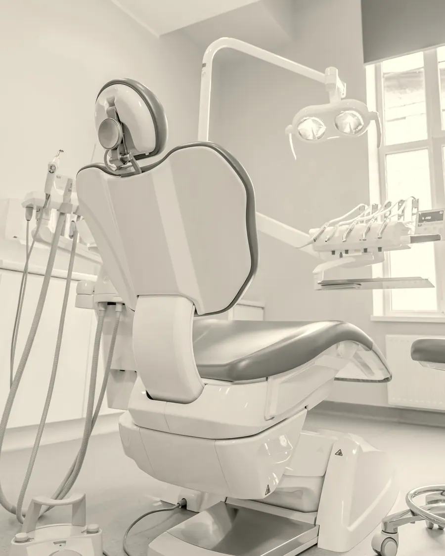 Consultório claro com cadeira odontológica branca junto a uma janela.